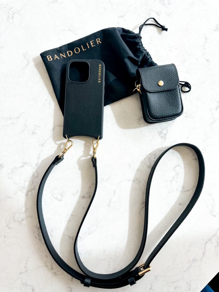 Black leather Bandolier crossbody phone case with gold hardware on a white background